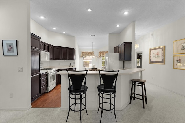 kitchen featuring white appliances, light carpet, a kitchen breakfast bar, dark brown cabinetry, and a peninsula