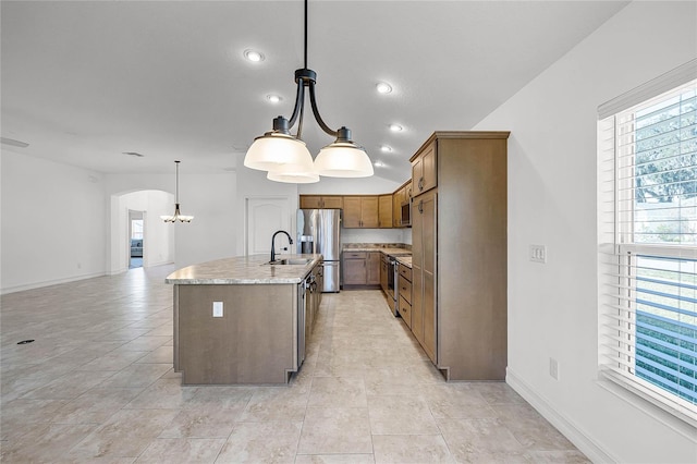 kitchen with a center island with sink, sink, hanging light fixtures, appliances with stainless steel finishes, and a notable chandelier