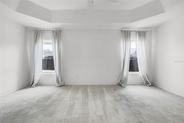 carpeted empty room with a tray ceiling, plenty of natural light, and ceiling fan