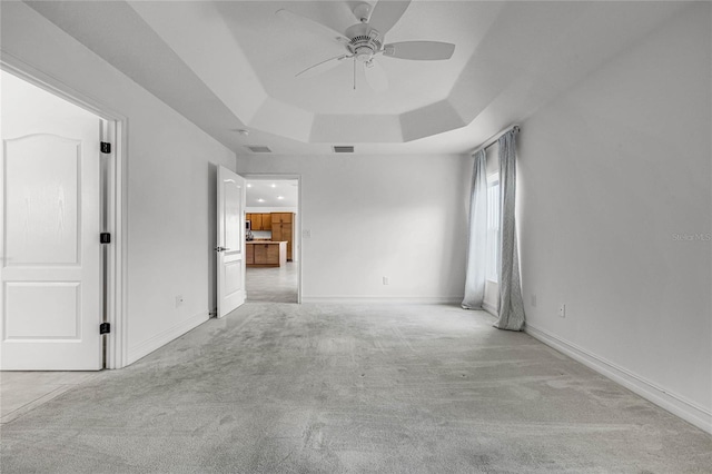 carpeted empty room featuring a raised ceiling and ceiling fan