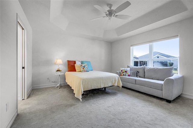 carpeted bedroom with ceiling fan and a tray ceiling