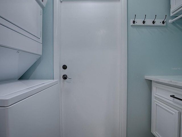 clothes washing area featuring cabinets and stacked washing maching and dryer