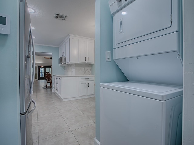 laundry room featuring light tile patterned floors, stacked washer and dryer, ceiling fan, and crown molding