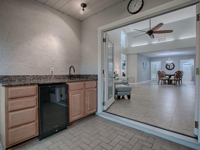 bar featuring ceiling fan, sink, hanging light fixtures, wine cooler, and dark stone countertops