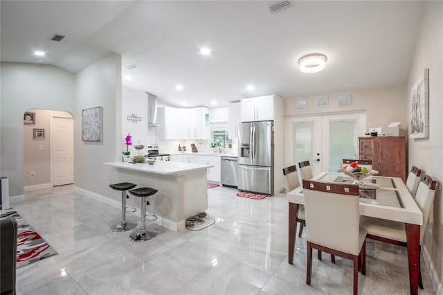 kitchen featuring kitchen peninsula, a kitchen breakfast bar, stainless steel appliances, wall chimney range hood, and white cabinets