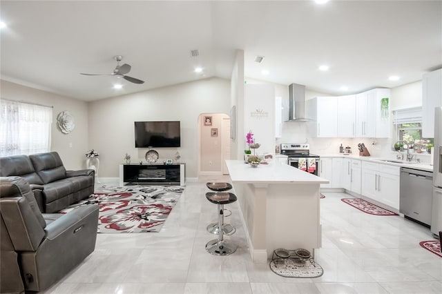 kitchen featuring wall chimney range hood, white cabinets, lofted ceiling, a kitchen island, and appliances with stainless steel finishes