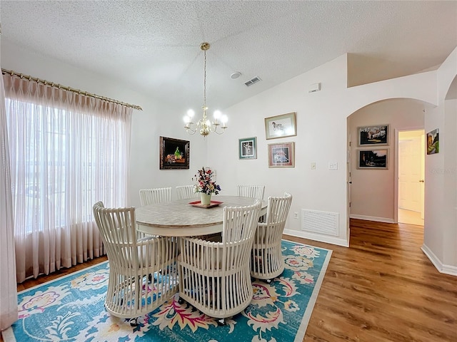 dining space featuring hardwood / wood-style floors, a notable chandelier, a textured ceiling, and vaulted ceiling