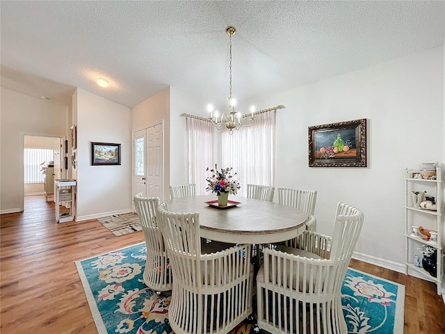 dining space with vaulted ceiling, hardwood / wood-style flooring, a textured ceiling, and a notable chandelier