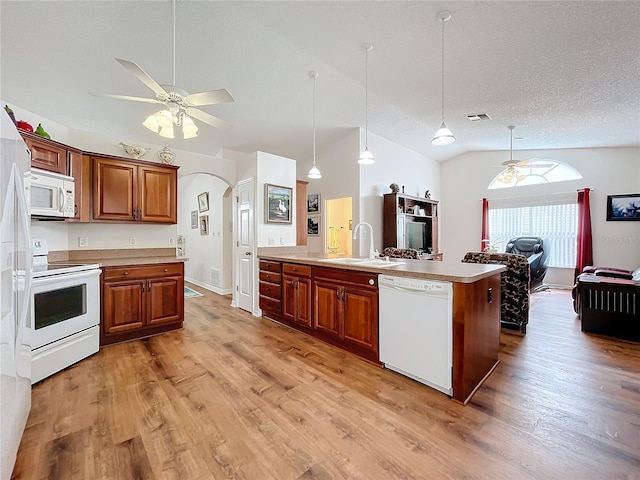 kitchen featuring sink, hanging light fixtures, an island with sink, vaulted ceiling, and white appliances