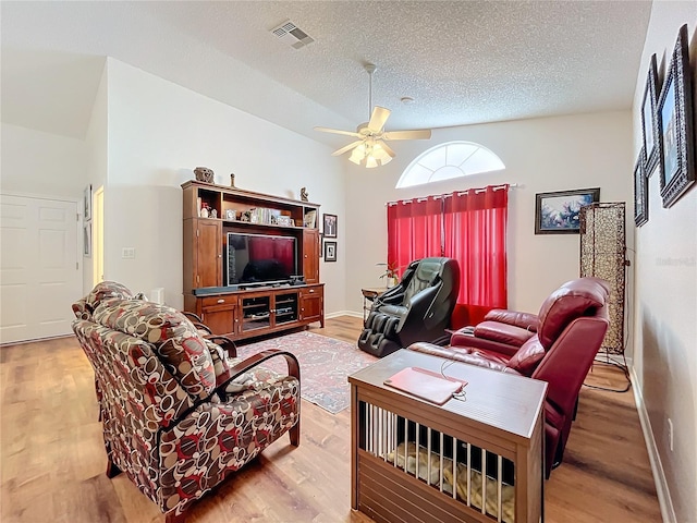 living room featuring a textured ceiling, light hardwood / wood-style floors, ceiling fan, and lofted ceiling