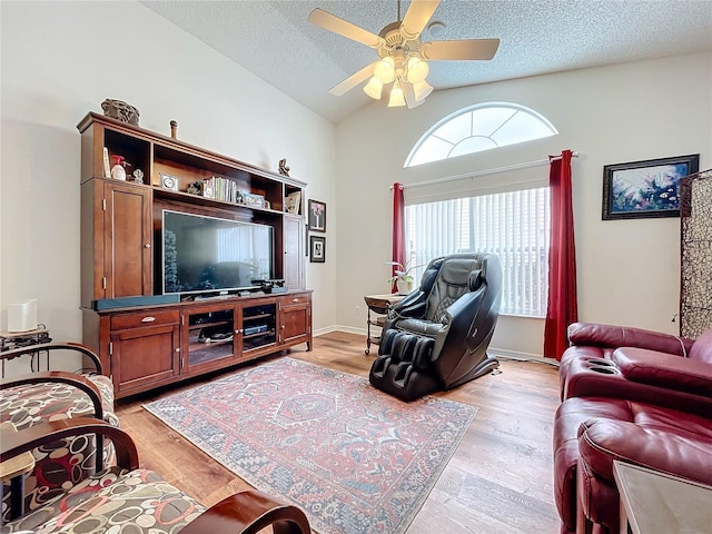 living room featuring ceiling fan, light hardwood / wood-style floors, lofted ceiling, and a textured ceiling