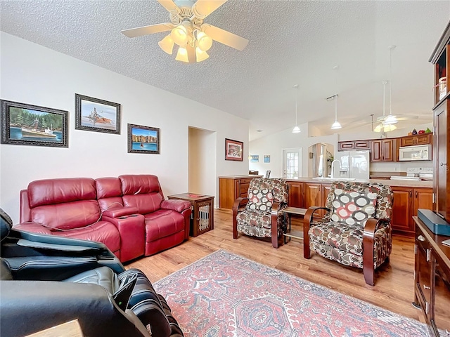 living room with vaulted ceiling, ceiling fan, a textured ceiling, and light wood-type flooring