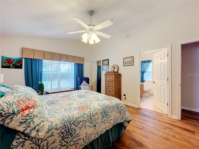 bedroom with ensuite bathroom, vaulted ceiling, ceiling fan, light wood-type flooring, and a textured ceiling