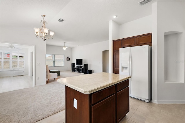 kitchen featuring ceiling fan with notable chandelier, a kitchen island, white refrigerator with ice dispenser, hanging light fixtures, and light colored carpet