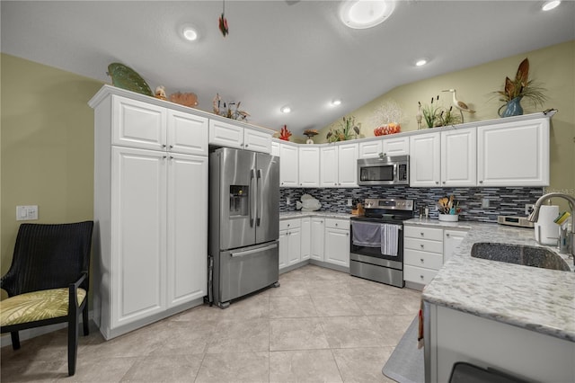 kitchen with sink, lofted ceiling, decorative backsplash, white cabinets, and appliances with stainless steel finishes