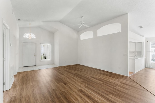 foyer entrance featuring sink, light hardwood / wood-style flooring, ceiling fan, high vaulted ceiling, and a textured ceiling