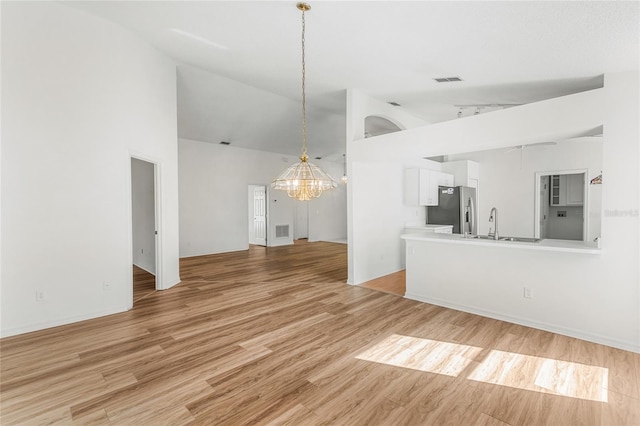 unfurnished living room featuring sink, high vaulted ceiling, a chandelier, and light wood-type flooring