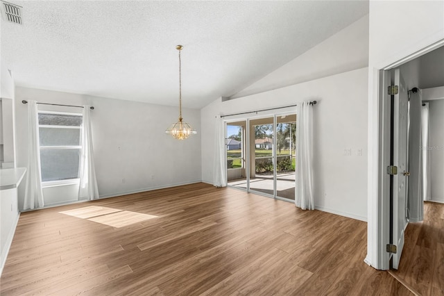 unfurnished dining area featuring lofted ceiling, a notable chandelier, hardwood / wood-style flooring, and a textured ceiling