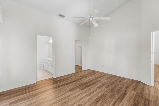 unfurnished bedroom with connected bathroom, a walk in closet, light hardwood / wood-style flooring, and high vaulted ceiling