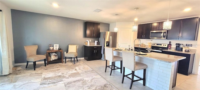 kitchen featuring dark brown cabinets, an island with sink, decorative light fixtures, and appliances with stainless steel finishes