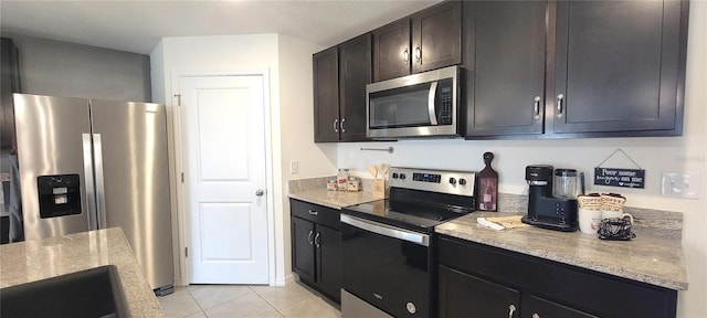 kitchen featuring dark brown cabinets, light stone countertops, light tile patterned floors, and appliances with stainless steel finishes