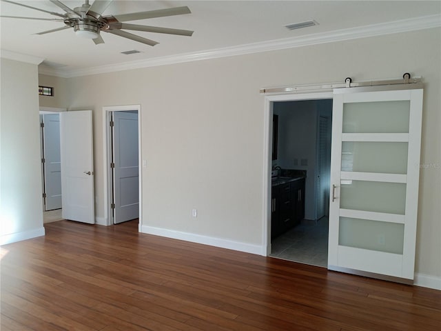 spare room with ceiling fan, a barn door, dark hardwood / wood-style floors, and ornamental molding