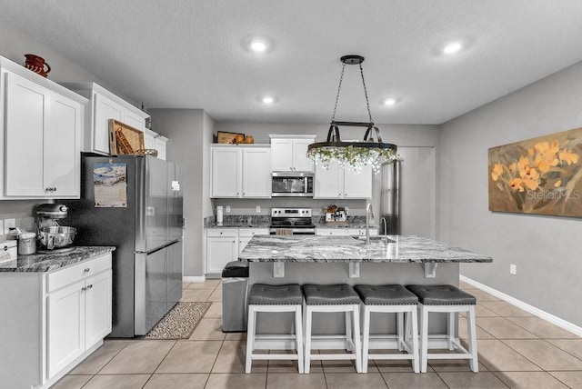 kitchen featuring appliances with stainless steel finishes, light stone counters, light tile patterned floors, white cabinets, and an island with sink