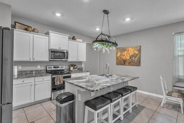 kitchen featuring hanging light fixtures, stainless steel appliances, dark stone countertops, an island with sink, and white cabinets