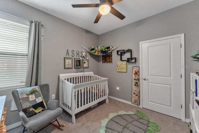 carpeted bedroom with ceiling fan and a crib