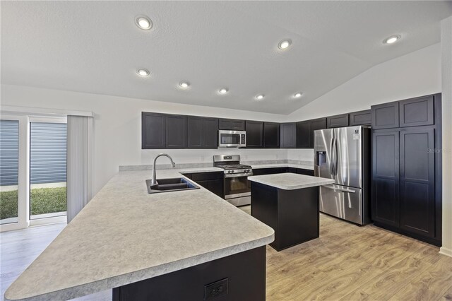 kitchen featuring kitchen peninsula, light wood-type flooring, stainless steel appliances, vaulted ceiling, and sink