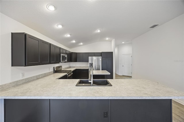 kitchen featuring sink, light hardwood / wood-style flooring, vaulted ceiling, appliances with stainless steel finishes, and kitchen peninsula