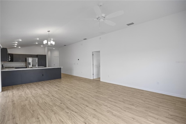 unfurnished living room featuring ceiling fan with notable chandelier, vaulted ceiling, and light hardwood / wood-style flooring