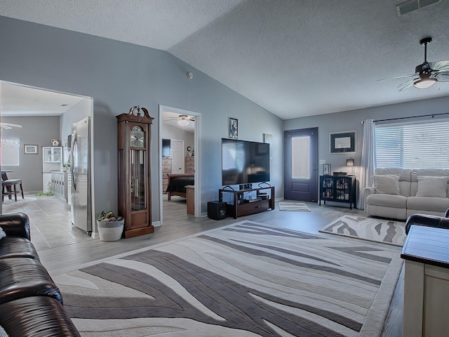 living room with vaulted ceiling, a textured ceiling, ceiling fan, and light hardwood / wood-style floors