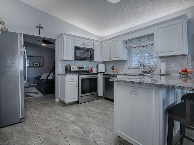 kitchen with lofted ceiling, white cabinets, stainless steel appliances, and ceiling fan