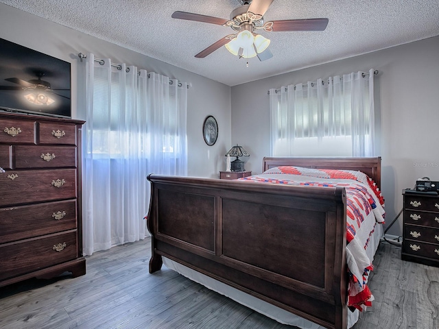 bedroom with ceiling fan, light hardwood / wood-style floors, and a textured ceiling