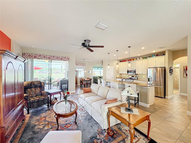 living room with a textured ceiling, ceiling fan, and light tile patterned flooring