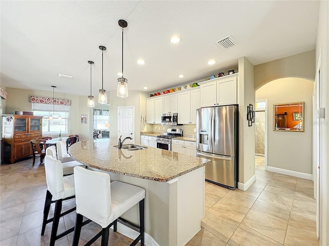 kitchen with light stone counters, stainless steel appliances, a center island with sink, white cabinets, and a breakfast bar area