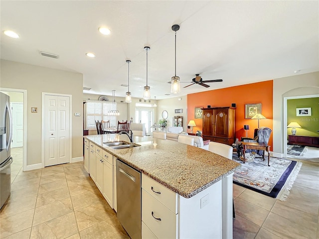 kitchen with a kitchen island with sink, sink, ceiling fan, light stone countertops, and appliances with stainless steel finishes