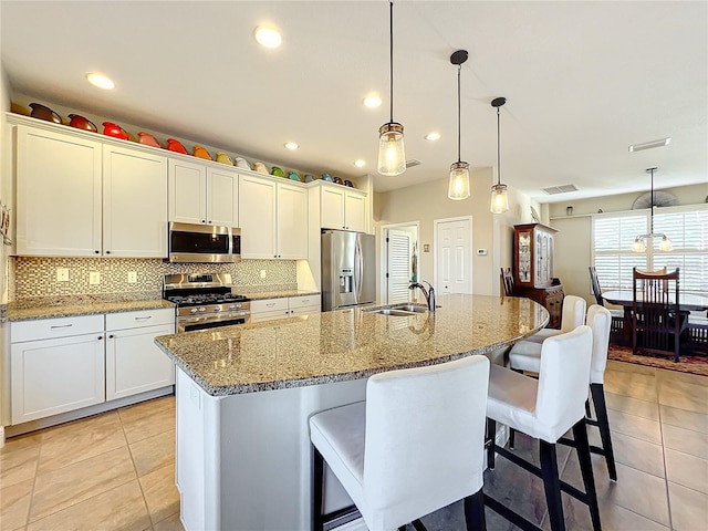 kitchen with sink, an island with sink, pendant lighting, white cabinets, and appliances with stainless steel finishes