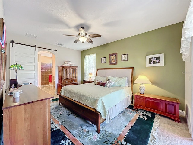 bedroom with ceiling fan, a barn door, carpet floors, and connected bathroom