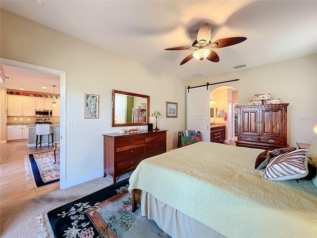 carpeted bedroom with a barn door, ceiling fan, and connected bathroom