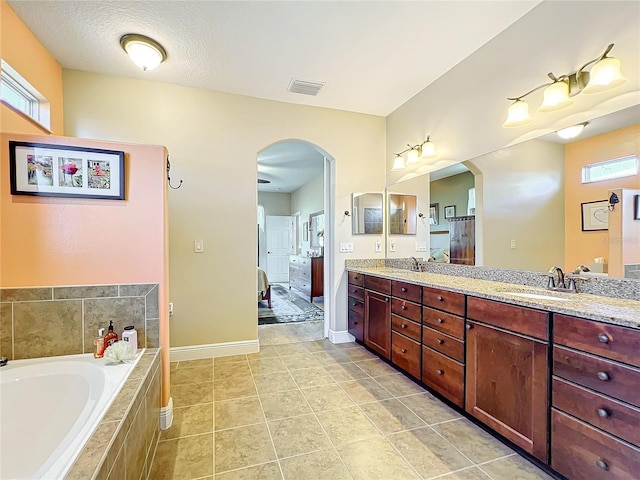 bathroom with tiled tub, tile patterned flooring, vanity, and a textured ceiling