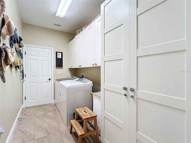 laundry room featuring cabinets, a textured ceiling, and washing machine and clothes dryer