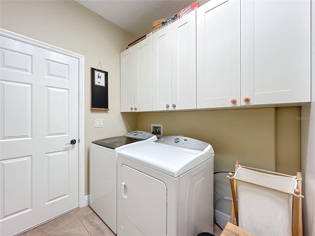 clothes washing area with washer and dryer, cabinets, and light tile patterned floors