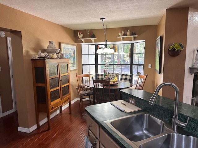 kitchen featuring a textured ceiling, sink, dark wood-type flooring, and decorative light fixtures