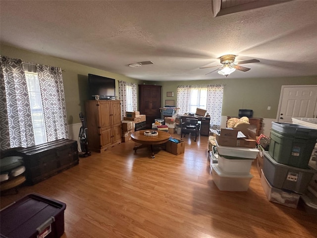 living room with ceiling fan, a textured ceiling, and light hardwood / wood-style flooring