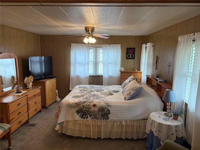 carpeted bedroom with ceiling fan and wood walls