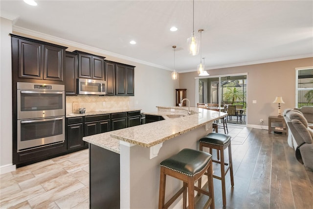 kitchen with pendant lighting, stainless steel appliances, a breakfast bar area, and an island with sink