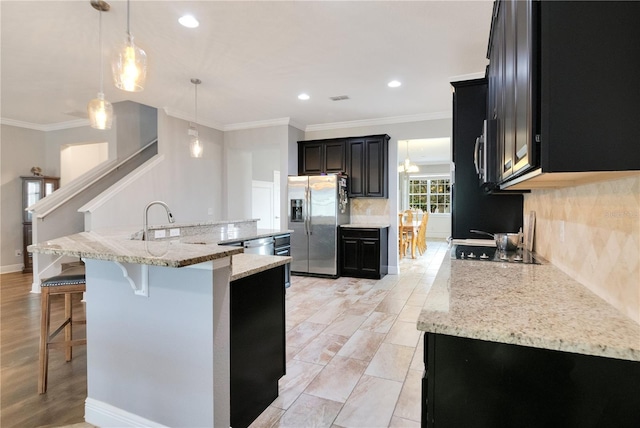 kitchen with decorative light fixtures, backsplash, a center island with sink, and stainless steel appliances