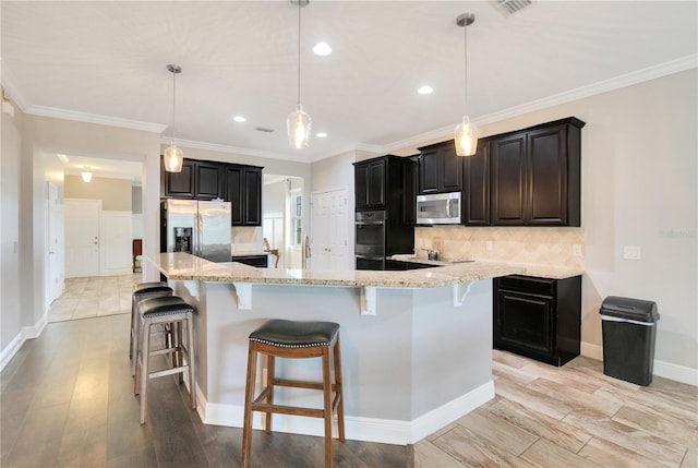 kitchen featuring appliances with stainless steel finishes, decorative backsplash, decorative light fixtures, light hardwood / wood-style flooring, and a large island with sink